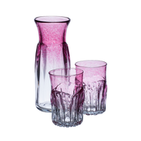 Carafe and two glasses with clear glass on the bottom and cranberry glass on the top. On a transparent background.