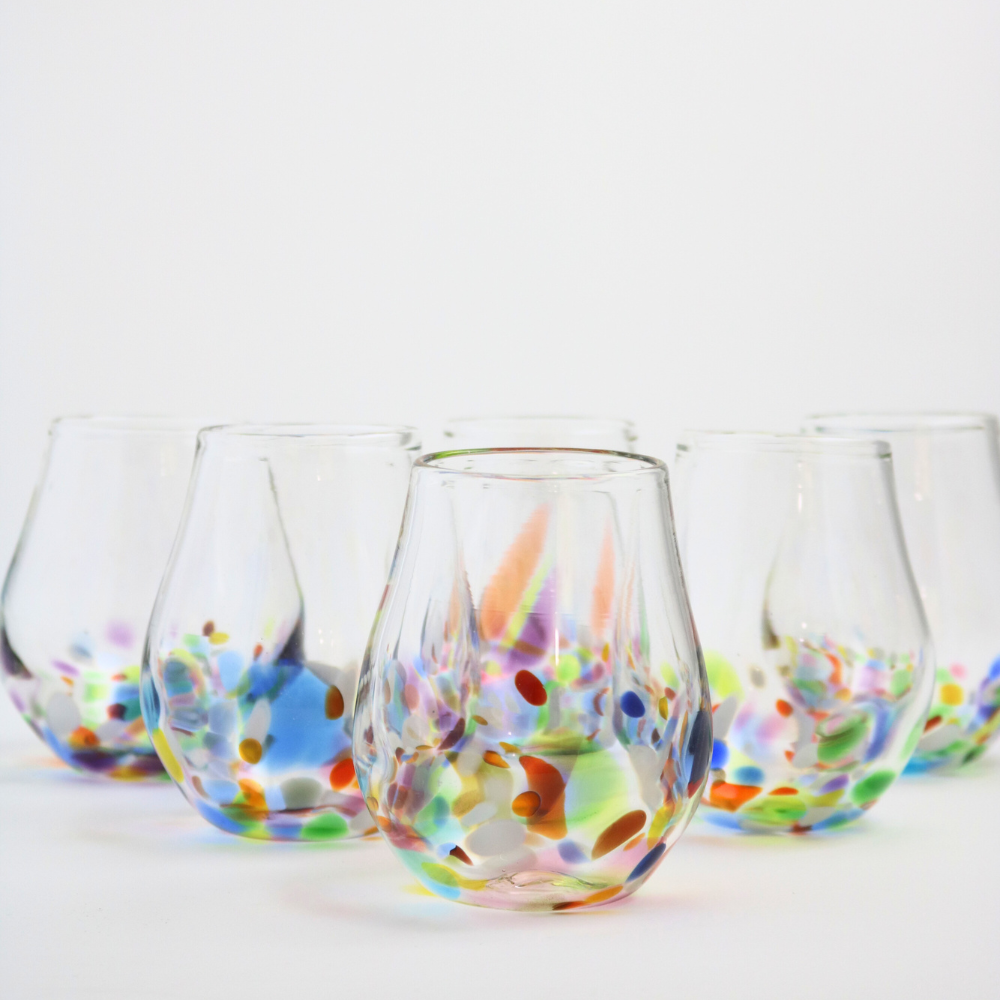 Several stemless wine glasses with colourful bottoms set up in a triangle