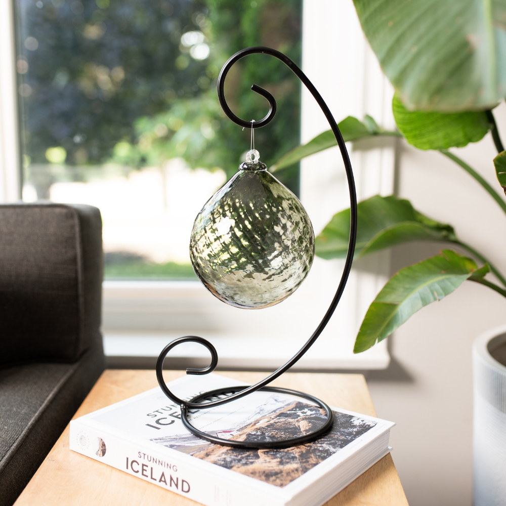 Pewter Enchanting Moonlight Radiance Orb on a Large Curved Single Ornament Holder resting on a white Iceland book with a window and green plant in the background