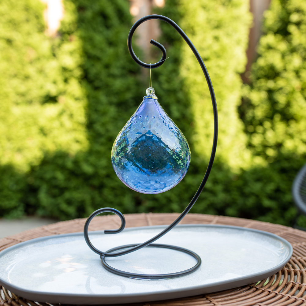 Cobalt Mystical Depths Orb on a Large Curved Single Ornament Holder, displayed on a white plate with green trees in the background