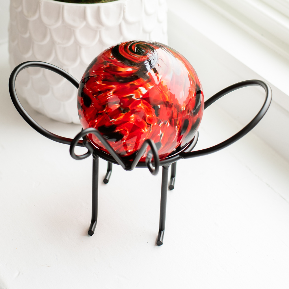 Red and black glass orb on a black insect garden holder on a white windowsill