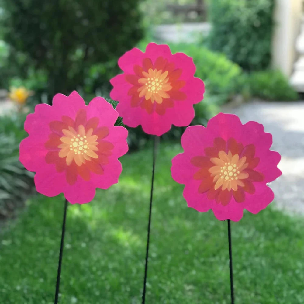 Three pink flower metal magnets with yellow centres on black garden stakes. 