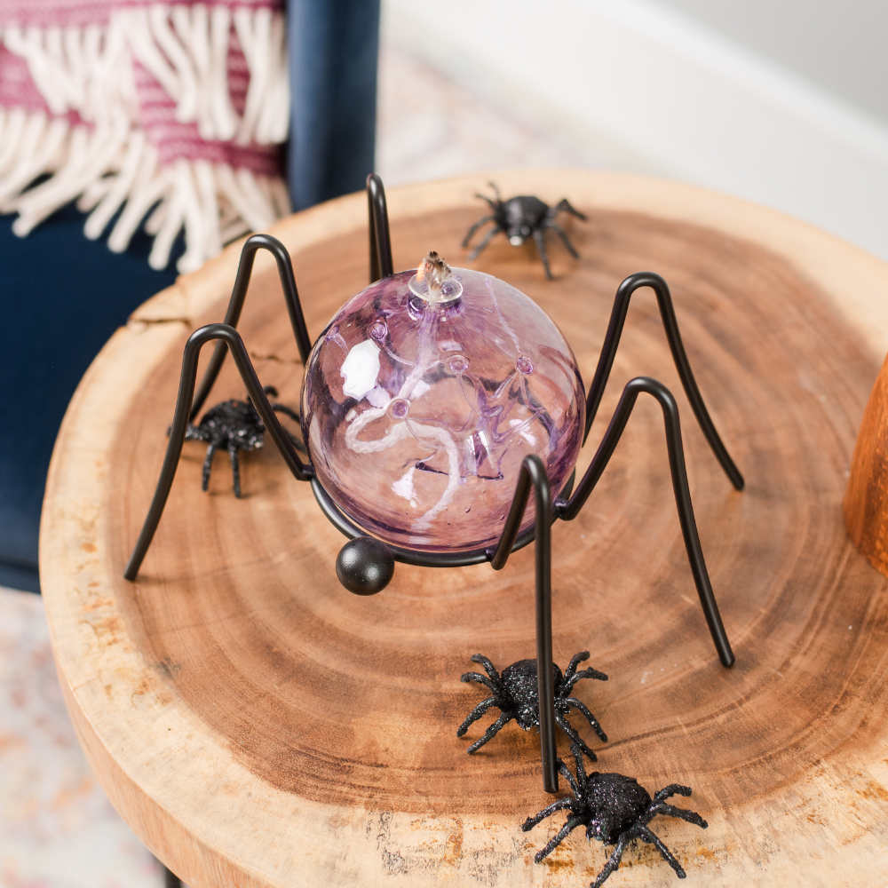 Amethyst Olde English Witch Ball Oil Lamp on a Spider Garden Holder. Displayed on a side table with fake spiders surrounding.