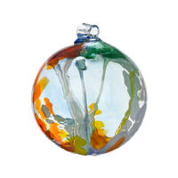 Glass orb with orange, white, yellow and green glass on the surface with white webbing pulled from bottom to top. On a transparent background.